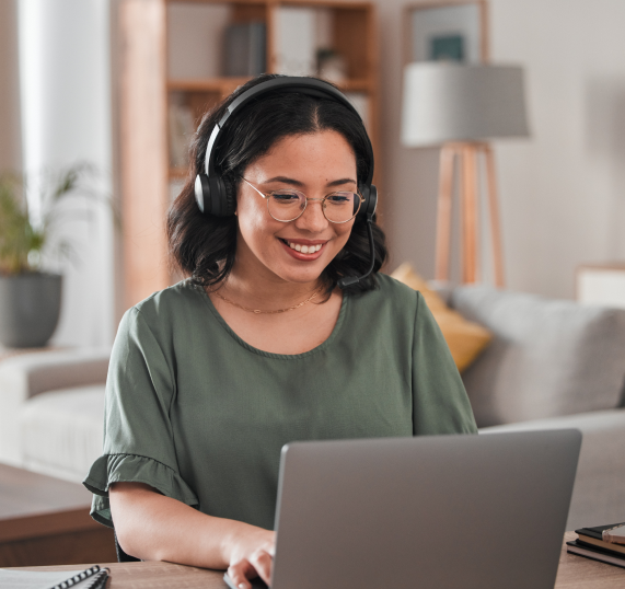 a woman in a living room sitting at a laptop with headphones on and smiling